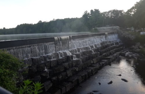 A serene waterfall cascading over a stone dam, surrounded by lush greenery and a calm river.
