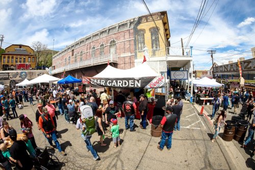 A bustling outdoor beer garden with tents, crowds of people, and a vibrant atmosphere under a blue sky.
