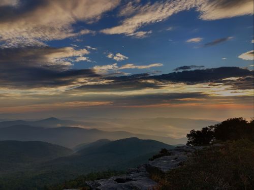 A scenic view of layered mountains under a colorful sunset sky with clouds and soft light.