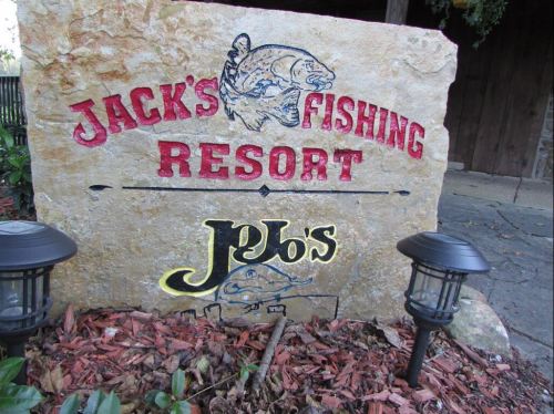 Sign for Jack's Fishing Resort featuring a fish graphic, surrounded by landscaping and outdoor lighting.