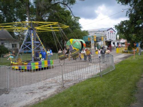 A colorful carnival scene with a swing ride, people enjoying the fair, and food stalls in the background.