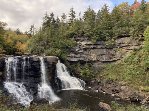 A scenic waterfall cascades over rocks, surrounded by lush greenery and autumn-colored trees.