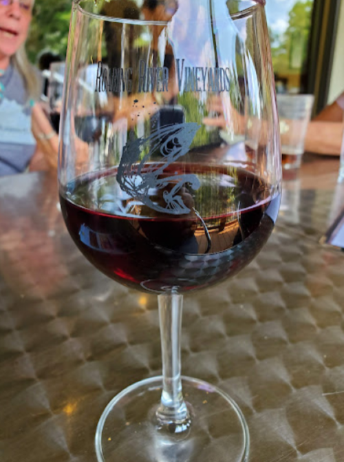 A glass of red wine with an etched design, sitting on a table with blurred people in the background.
