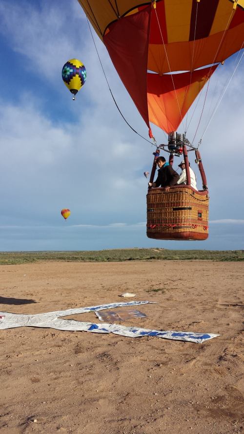 A colorful hot air balloon prepares for takeoff, with other balloons in the background against a clear sky.