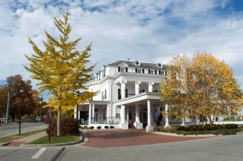 A large white building with columns, surrounded by autumn trees with yellow leaves under a cloudy sky.