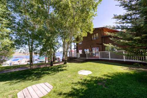 A scenic view of a lakeside cabin surrounded by trees and a grassy area, with a dock visible in the background.