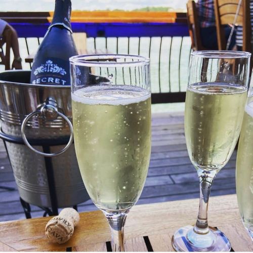 Two flutes of sparkling wine on a wooden table, with a bottle and ice bucket in the background. A cork lies nearby.