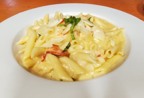 Creamy pasta dish with penne, cheese, and fresh basil, served in a white bowl on a wooden table.