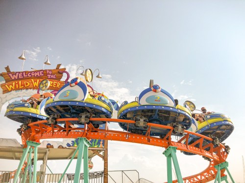 Colorful roller coaster cars on a track with a "Welcome to the Wild Wonder" sign in the background.