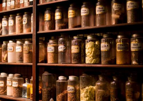 A wooden shelf filled with various glass jars of spices and herbs, each labeled with handwritten tags.