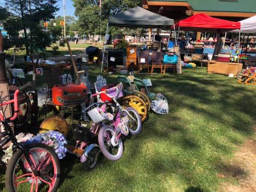A vibrant outdoor market scene with colorful tents, vintage items, and bicycles lined up on the grass.