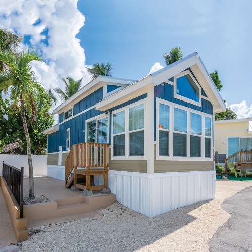 A colorful beach house with a porch, surrounded by palm trees and a clear blue sky.