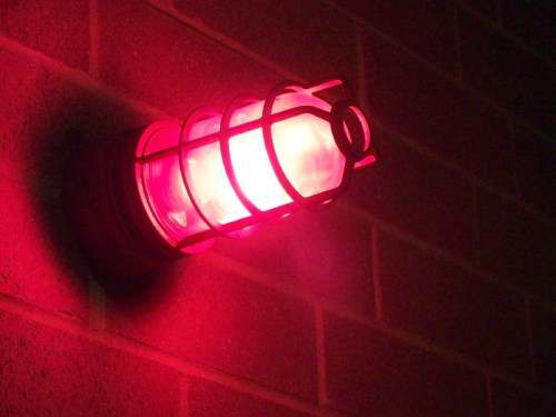 A red industrial light fixture mounted on a brick wall, emitting a soft glow.