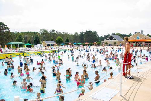 A crowded water park pool with many people enjoying the water, while a lifeguard watches from the side.