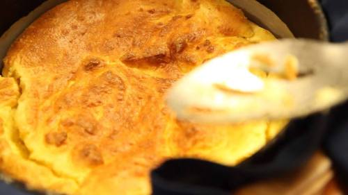 A golden-brown baked dish in a pot, with a spoon resting beside it, suggesting a delicious, fluffy texture.