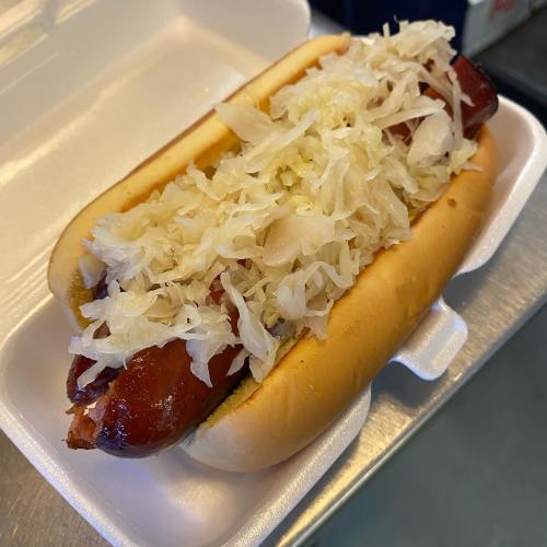 A hot dog in a bun topped with sauerkraut, served in a takeout container.