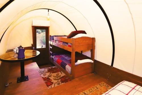 Cozy interior of a glamping tent featuring bunk beds, a table, and a window with a view.
