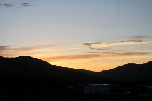 A serene sunset over rolling hills, with soft orange and purple hues in the sky and a silhouette of mountains.