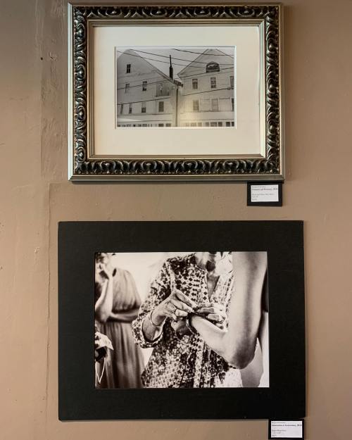 Two framed black-and-white photographs hang on a wall; one shows a building, the other depicts hands in a social setting.