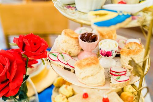 A tiered tray of assorted pastries, scones, and radish slices, with red roses in the foreground.