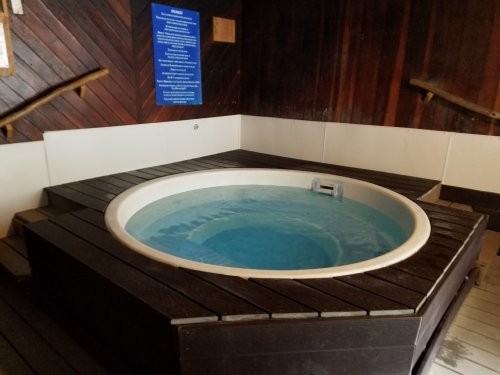 A circular hot tub with clear water, surrounded by wooden decking in a cozy indoor setting.