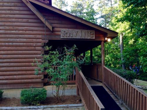 A wooden cabin entrance with a sign reading "RAVINE" and a pathway leading to the door, surrounded by greenery.