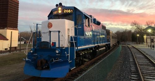 A blue locomotive with the number 2661 parked on tracks during sunset, with a building in the background.