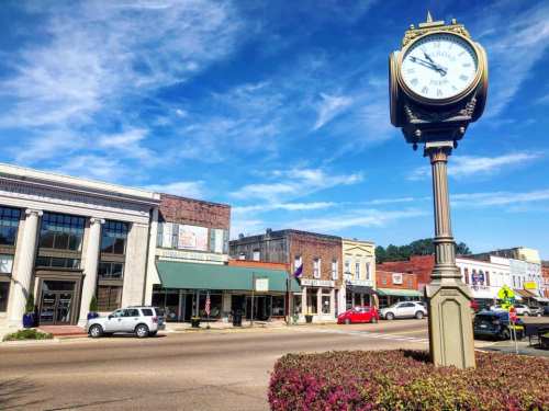 A charming small town street with historic buildings, a clock tower, and clear blue skies.