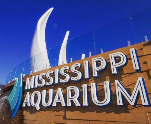 Signage of the Mississippi Aquarium with a blue sky in the background and modern architectural elements.