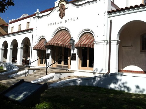 Exterior of Quapaw Baths, featuring arched entryways, striped awnings, and a sunny blue sky.