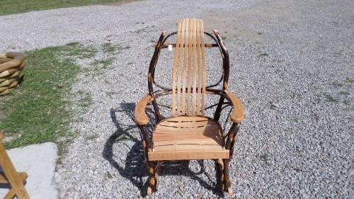 A wooden rocking chair with a slatted seat and backrest, set on a gravel surface with grass in the background.