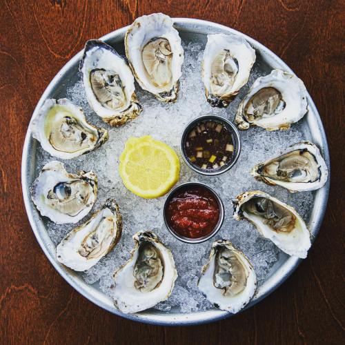 A platter of fresh oysters on ice, served with lemon and two dipping sauces.