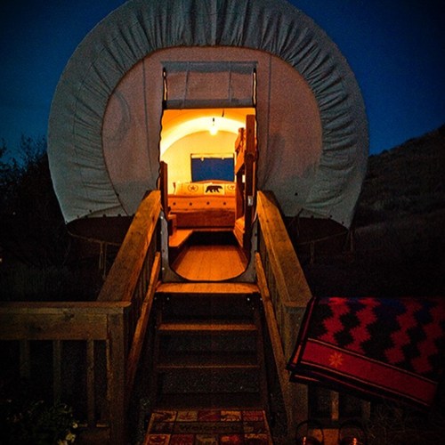 A cozy, illuminated wagon entrance at night, with wooden steps and a colorful blanket nearby.