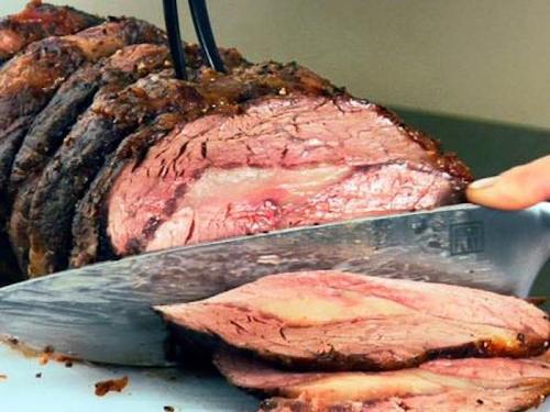 A close-up of a perfectly cooked roast beef being sliced, showcasing its juicy, pink interior and crispy outer layer.