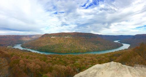 A panoramic view of a winding river surrounded by autumn-colored hills under a cloudy sky.
