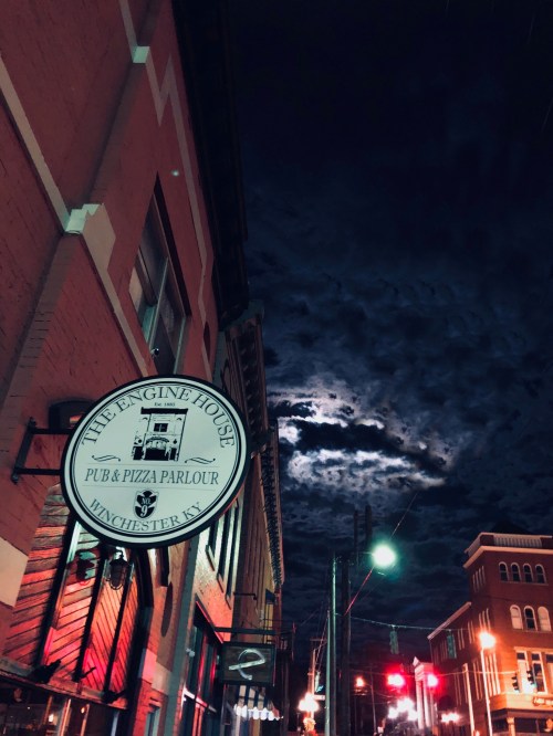 A pub sign illuminated at night, with a dramatic cloudy sky and moon in the background.
