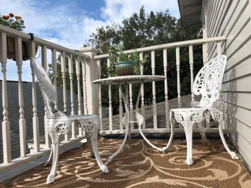 A small balcony with a round table and two white chairs, surrounded by a railing and a potted plant on the table.