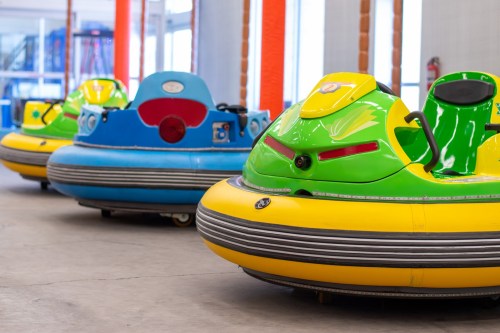 Colorful bumper cars lined up in an indoor amusement area, featuring bright yellow, green, and blue designs.