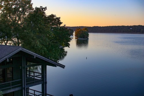 A serene lake at sunset, with trees reflecting on the calm water and a cabin in the foreground.