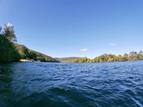 A serene river scene with clear blue water, lush green banks, and a bright blue sky dotted with a few clouds.