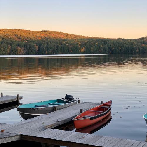 Canoes docked at a serene lake with autumn foliage reflecting on the water at sunset.