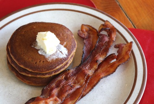 A plate with three pancakes topped with butter and a side of crispy bacon strips.