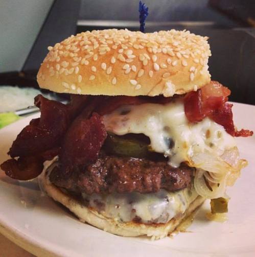 A juicy burger with melted cheese, crispy bacon, pickles, and grilled onions, served on a sesame seed bun.