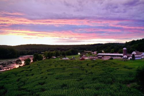 A scenic farm at sunset, featuring fields, a barn, and a river under a colorful sky with pink and purple hues.