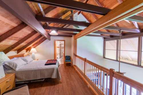 Cozy loft bedroom with wooden beams, a bed, and a small seating area, featuring warm lighting and a welcoming atmosphere.