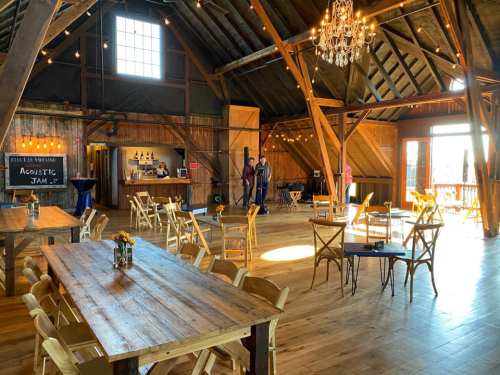 A spacious rustic venue with wooden beams, tables, and chairs, featuring a bar area and warm lighting.