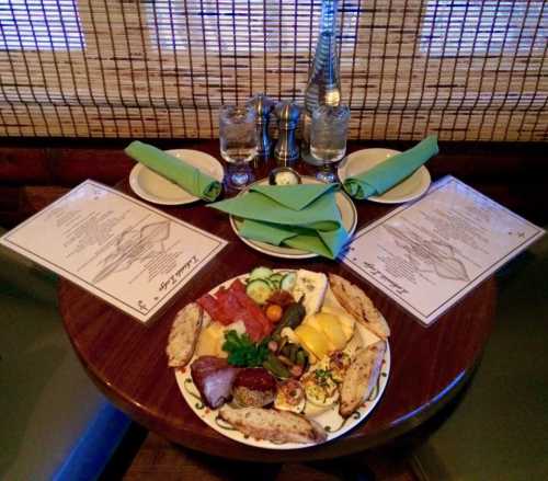 A table set for dining with two menus, glasses of water, and a platter of assorted meats, cheeses, and vegetables.