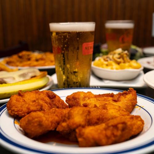 A plate of crispy fried chicken wings in front of a glass of beer, with side dishes in the background.