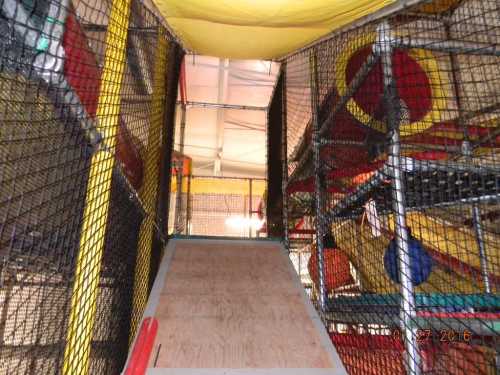 A view of a colorful indoor play structure with netting, slides, and climbing areas.