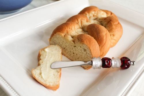 A loaf of bread on a white plate, with a slice cut and a butter knife beside it.